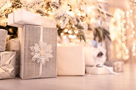 Christmas gifts box under tree with artificial snow with golden illumination. Silver colorの写真素材