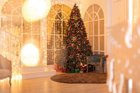Interior Christmas tree decorated with red balls, stars, illuminations, gifts lie belowの写真素材