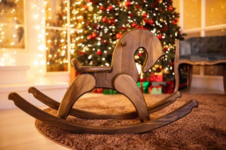 Wooden children chair in shape of horse against background of Christmas tree with illuminationの写真素材
