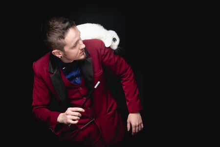 Magician man makes trick with white rabbit and magic wand, copy space black backgroundの写真素材
