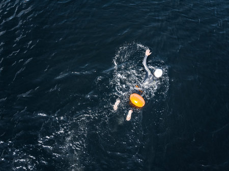 Arctic people swim ice hole in cold water, athletes in wetsuits with orange buoys in blue sea
