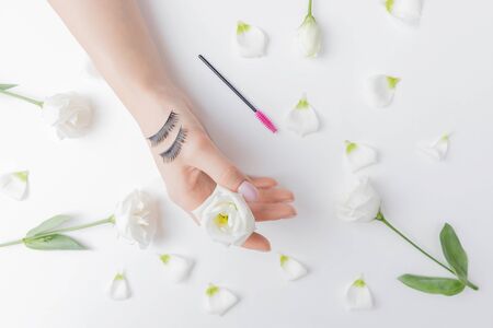 False eye lashes on hand woman master extension white flowers on background. Concept beauty fashionの写真素材