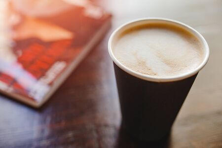 Top view texture of foam and coffee cappuccino latte bubbles in paper cup on wooden table, lens flare, background is magazineの写真素材