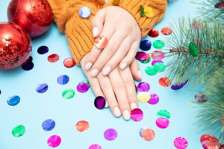 Female beautiful hands with manicure on nails in warm sweater with red Christmas ball new year on blue background. Top view.の写真素材