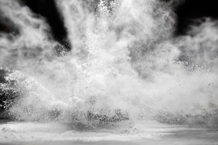 White flour flies in air on black background, pastry chef claps hands and prepares yeast dough for...