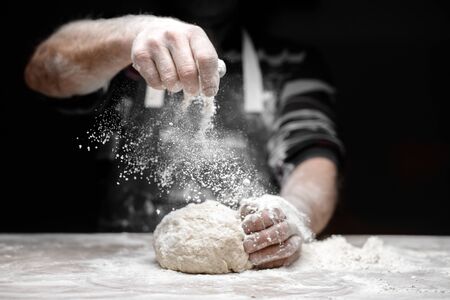 White flour flies in air on black background, pastry chef claps hands and prepares yeast dough for pizza pasta.の写真素材