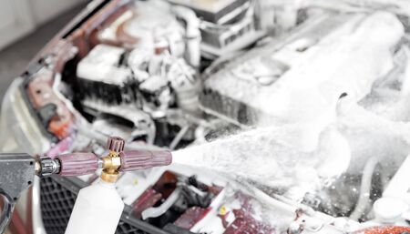 Service car wash, woman master spray foam to clean engine from dirtの写真素材