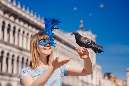 Portrait smiling young woman in Venice, Italy in Venetian mask holding pigeons on St Mark Square. Concept travelの写真素材