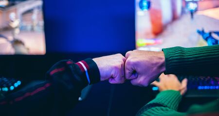 Professional gamer greeting and support team fists hands online game in neon color blur background. Soft focus, back viewの写真素材