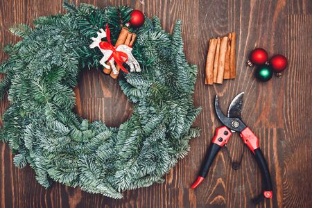 Top view florist making Christmas wreath on wooden table, flat lay tree branches secateurs, deer with red scarfの写真素材