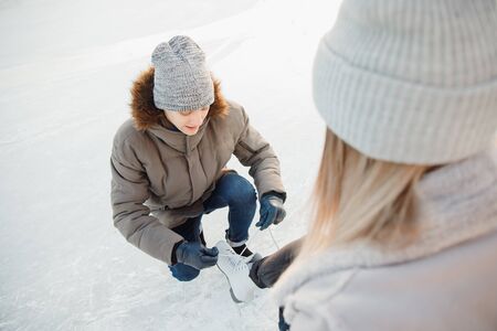Man helps to put on white figure skates for rink to beautiful young girl on background of snow in winter, concept is care love, relationship between people.の写真素材