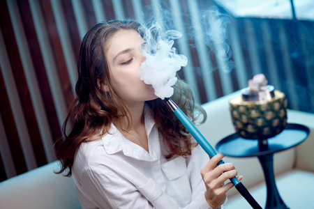 Young beautiful woman in night club smoke hookah or shisha bar, blue background