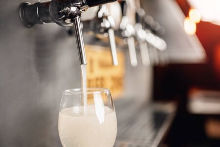 Barman pours light alcoholic cider of keg tap into glass. Dark backgroundの写真素材