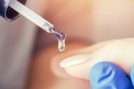 Macro photo manicure drop of varnish, master applies gel with brush on nails of girl.の写真素材