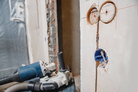 Builder worker cutting electrical chase in concrete wall with circulation saw drill diamond crown.の写真素材