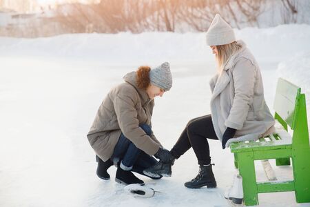 Man helps to put on white figure skates for rink to beautiful young girl on background of snow in winter, concept is care love, relationship between people.の写真素材