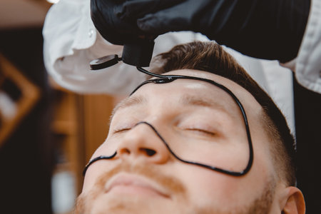 Barber applies black charcoal mask to man face to clean pore skin and remove acne from nose, spa...