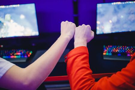 Professional gamer greeting and support team fists hands online game in neon color blur background. Soft focus, back view.の写真素材