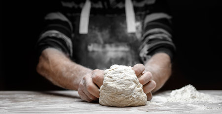Hands of male baker preparing yeast dough with white flour dust on black background, scoop out for...