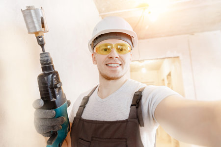 Builder worker man makes selfie photo with safety glasses and white helmet with pneumatic hammer...