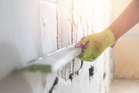 Worker builder gray wall with applied gypsum plaster to smooth surface. Apartment repair concept.
