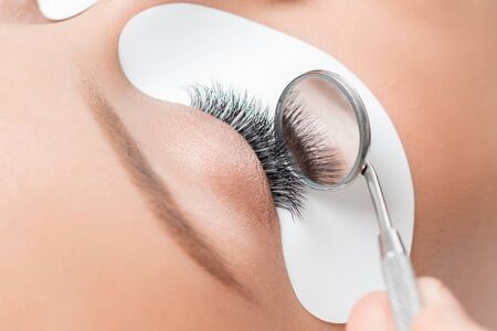 Macro eyelash extension procedure. Woman master combs lashesの写真素材