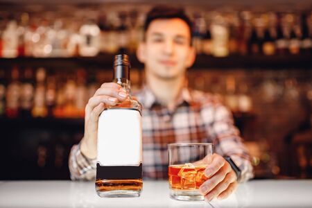 Barman holds out glass of whiskey with ice to male visitor. Concept rest in barの写真素材