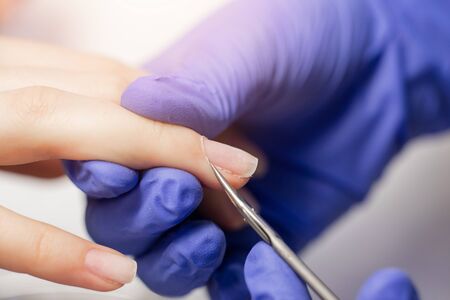 Manicurist uses scissors tool to cut cuticle on nails of client girl.の写真素材