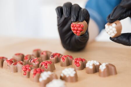 Confectioner in black gloves makes sweet heart-shaped chocolates with red and white fillingの写真素材