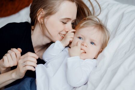 Happy family, young woman mother kisses baby in bedの写真素材