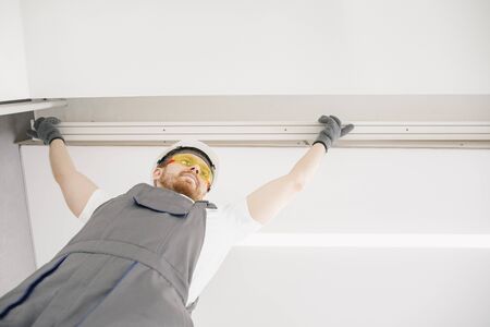 Male builder carpenter installs curtain on ceiling, bottom viewの写真素材