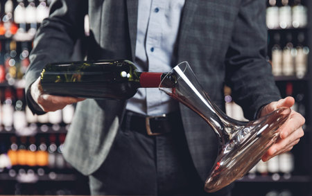 Sommelier pouring red wine into carafe decanter to make aeration drink.