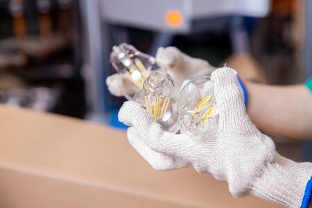 Worker hands picks up electric glass lamp, put cap on wiresの写真素材