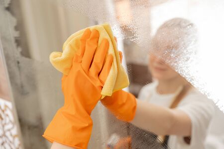 Woman cleans mirror from pollution and plaque from water in bathroomの写真素材