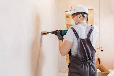 Builder worker pneumatic hammer drills hole in concrete brick wall with diamond crown for electric cable, socket, switch.の写真素材