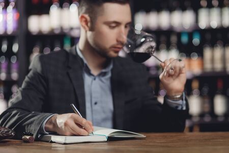 Sommeliers male hold glass red wine tasting and making notes degustation cardの写真素材