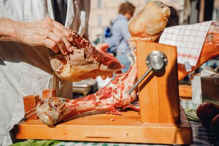 Male butcher cuts dried pork leg prosciutto ham with knife in center of Rome. Italy.の写真素材