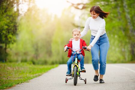 Mom teaches little son to ride bike in park, keep balance, have fun family. Mother day conceptの写真素材