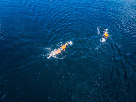 Arctic people swim ice hole in cold water, athletes in wetsuits with orange buoys in blue sea