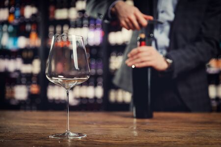 Close-up tasting glass goblet in background of sommelier opens with corkscrew cork of bottle of red wine.の写真素材