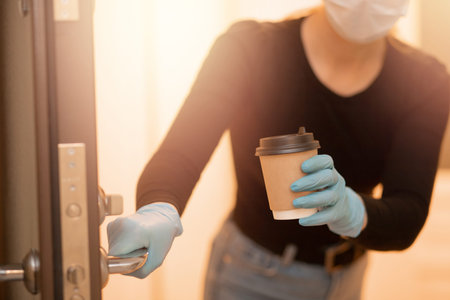 Delivery woman holding coffee and boxes cardboard in medical mask and rubber gloves. Quarantine...