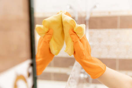 Woman cleans mirror from pollution and plaque from water in bathroomの写真素材