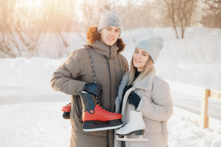 Loving couple or friends are looking into frame, holding skates for rink against backdrop of snow...