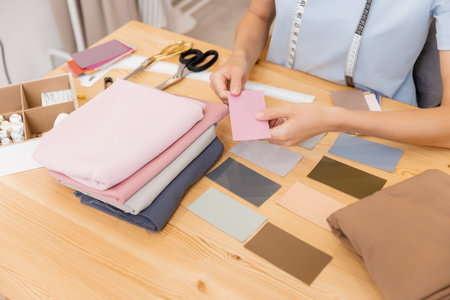 Young woman tailor fashion designer chooses shades of fabric and forms palette for tailoring...