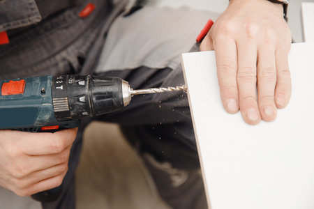 Kitchen installation, worker tightens bolts to assemble box from chipboardの写真素材