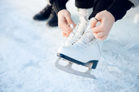Girl ties shoelaces on white figure skates for ice rink in winter. Christmas holidays conceptの写真素材