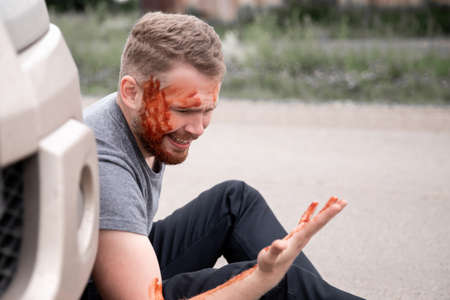 Insurance concept. Car accident, man sits with bloodied head near the wheel, cry for help in troubleの写真素材