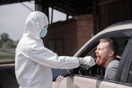 Concept ban driver car travel coronavirus. Doctor in protective virus suit taking swab from man to test for COVID-19 infectionの写真素材