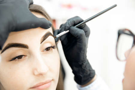 Beauty salon, master corrects and dyes eyebrows hair of young womanの写真素材