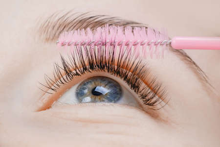 Eyelash extension procedure. Woman master combs lashes fakeの写真素材